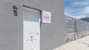Une porte blanche avec une petite plaque au-dessus, un mur à la texture particulière et un chemin pavé.