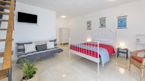 Une chambre avec un lit, un canapé, une télévision, une plante et une échelle.