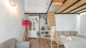 Een ruimtelijk ingerichte leefruimte met een hoogslaper, een slaapbank, een kitchenette en een ladder.