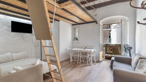 Een kamer met een houten plafond, een witte bank, een eettafel met stoelen en een ventilator.