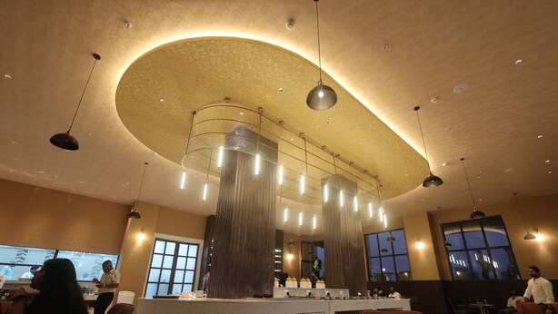 Un interior de restaurante moderno con una isla central, iluminación colgante y ventanas amplias.