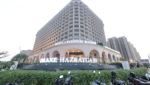 Un hotel grande de varios pisos llamado "OMAXE HAZRATGANI HOTEL CELESTIAL MANOR", con una entrada en arco destacada y numerosos balcones.