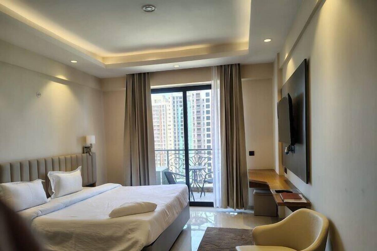 A modern hotel room with a large bed, a desk, a chair, and a TV on the wall.