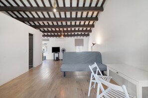 Una sala de estar moderna con un sofá gris, sillas blancas, una consola blanca, un televisor y un ventilador de techo.