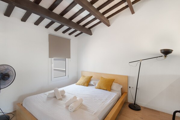 Un dormitorio con cama de madera, un ventilador de pie, una lámpara de pie y una ventana con persiana.