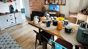A modern kitchen with a dining area, a TV, and a brick wall.