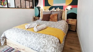 A modern bedroom with a bed, wooden headboard, bedside tables, and a colorful abstract wall art.