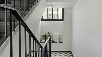 Un escalier avec des rampes noires, une fenêtre donnant sur des immeubles et un radiateur fixé au mur.