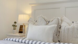 Una cama bien hecha con ropa de cama a rayas, un cabecero blanco y una mesita de noche con una lámpara y una planta pequeña.