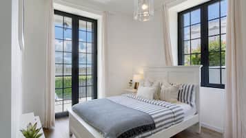 Une chambre à coucher avec un lit, une table de chevet, une lampe et de grandes fenêtres.
