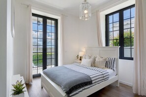 Un dormitorio con cama, mesita de noche, lámpara y ventanas amplias.