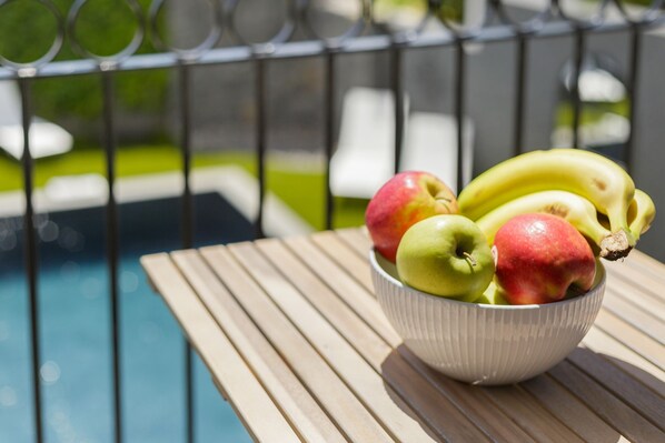 Un cuenco de fruta sobre una mesa de madera cerca de una piscina.