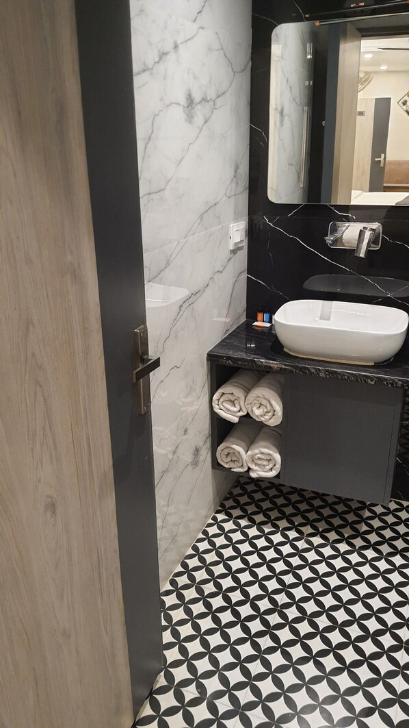 Un baño con pared de mármol, un lavabo, un espejo y suelo estampado.