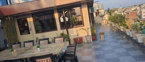 A rooftop terrace with a checkered floor, potted plants, and a table with chairs.