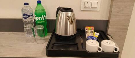 A breakfast tray with a coffee pot, two cups, a box of cereal, and two bottles of water and soda.