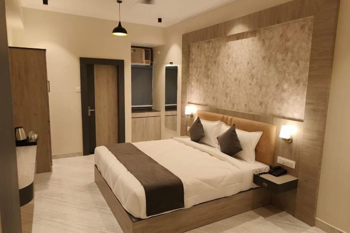 Una habitación de hotel moderna con una cama grande, mesitas de noche, un armario y un cabecero empotrado con iluminación integrada.