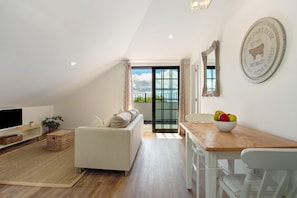 A modern living room with a sofa, a dining table with chairs, a television, and a wall-mounted mirror.