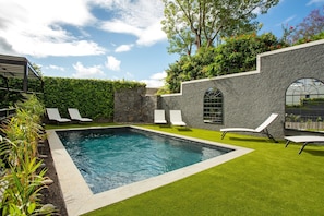 A swimming pool with a stone wall, white lounge chairs, and a grassy area. - Studio Apartment '6' with Sea View, Shared Pool and Wi-Fi Access (Funchal)