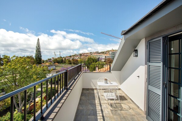 A balcony with a view of a town, a table, and a chair.