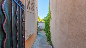 A narrow alleyway with a metal gate, a concrete path, and a building with a white door and shutters. - Studio Apartment 'Chez Lina -  Avec Terrasse' with Private Terrace and Wi-Fi (Le Lavandou)