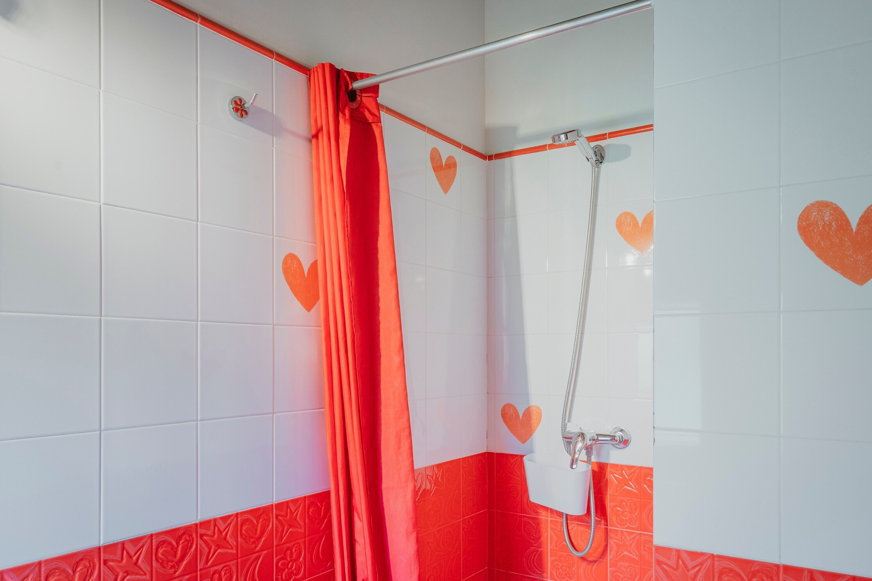 A shower with a red curtain and a handheld showerhead.