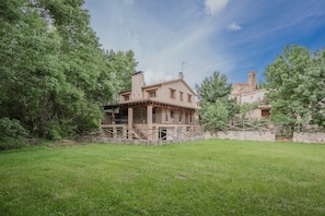 A rustic house with a stone wall and a wooden fence, surrounded by lush green trees.