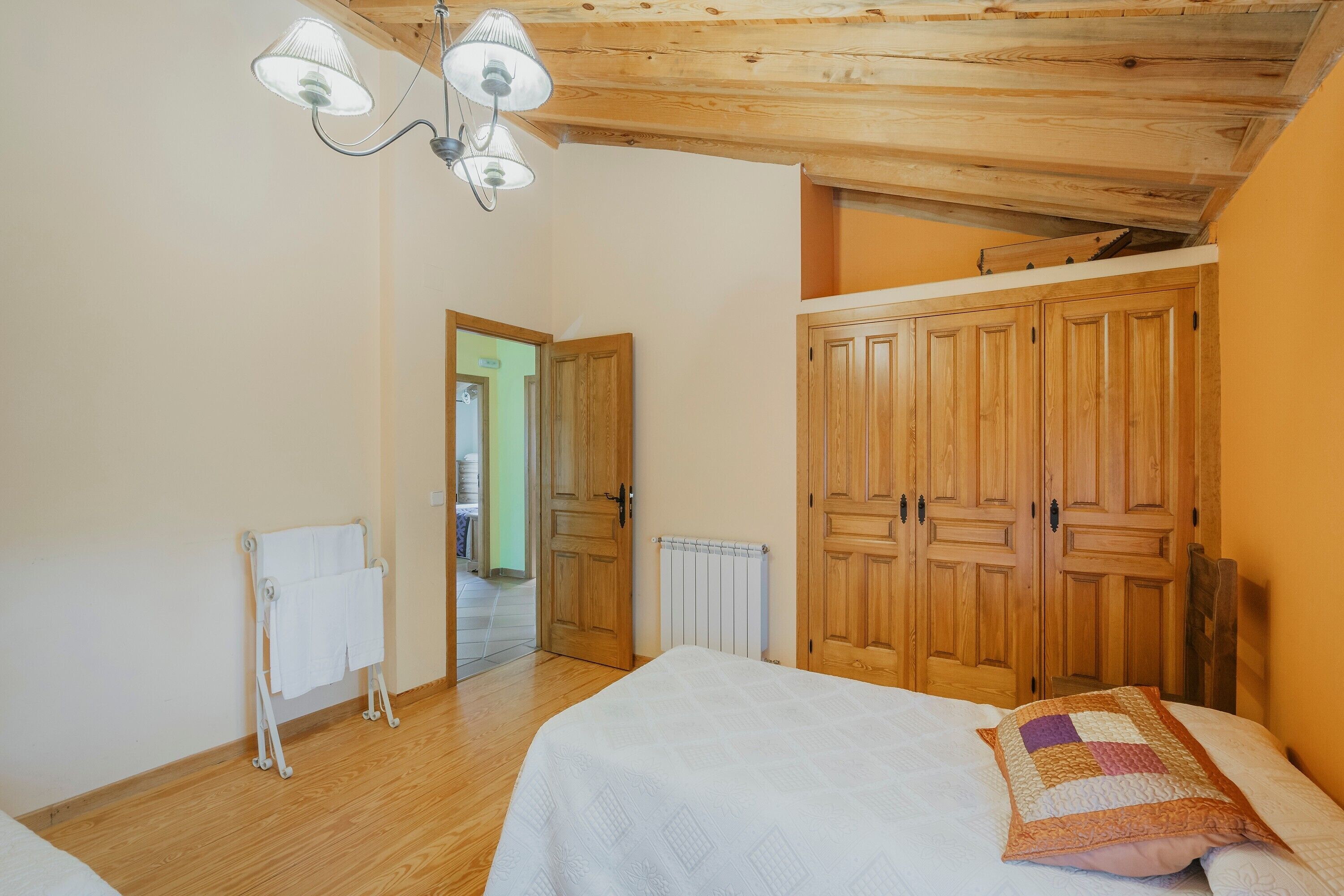 A bedroom with a wooden ceiling, a bed with a quilt, a radiator, and a wardrobe.