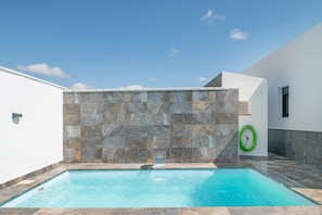 A swimming pool with a stone wall backdrop, a hose, and a window.