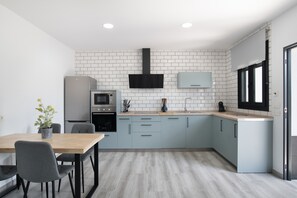 A modern kitchen with white brick backsplash, grey cabinets, a wooden dining table, and a built-in oven.