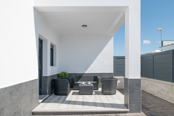 A modern outdoor patio with wicker furniture, a small table, and a potted plant.