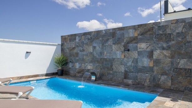 A swimming pool with a stone wall, a potted plant, and lounge chairs. - Holiday Home 'El Rincón Del Sur 2' with Private Pool, Wi-Fi and Air Conditioning (Barrio Nuevo)
