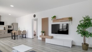 A modern living space with a dining area, a TV mounted on a wooden panel, a large potted plant, and a kitchen in the background. - Holiday Home 'El Rincón Del Sur 2' with Private Pool, Wi-Fi and Air Conditioning (Barrio Nuevo)