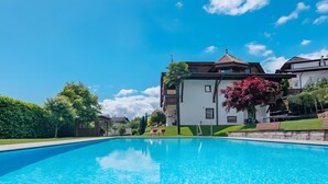 A swimming pool with a clear blue sky, a white building with a red roof, and green landscaping. - Apartment 'Christine 1' with Mountain View, Shared Pool and Wi-Fi (Riffian)