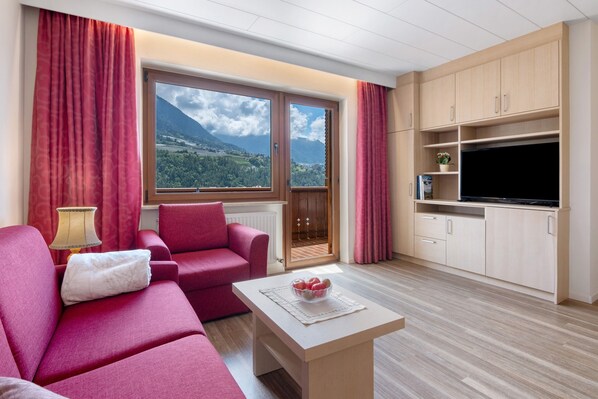 A living room with a sofa, a coffee table, a TV, and a window with a mountain view.
