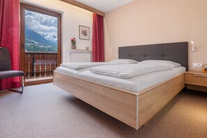 A bedroom with a large bed, a chair, a nightstand, and a view of a mountain through a window.