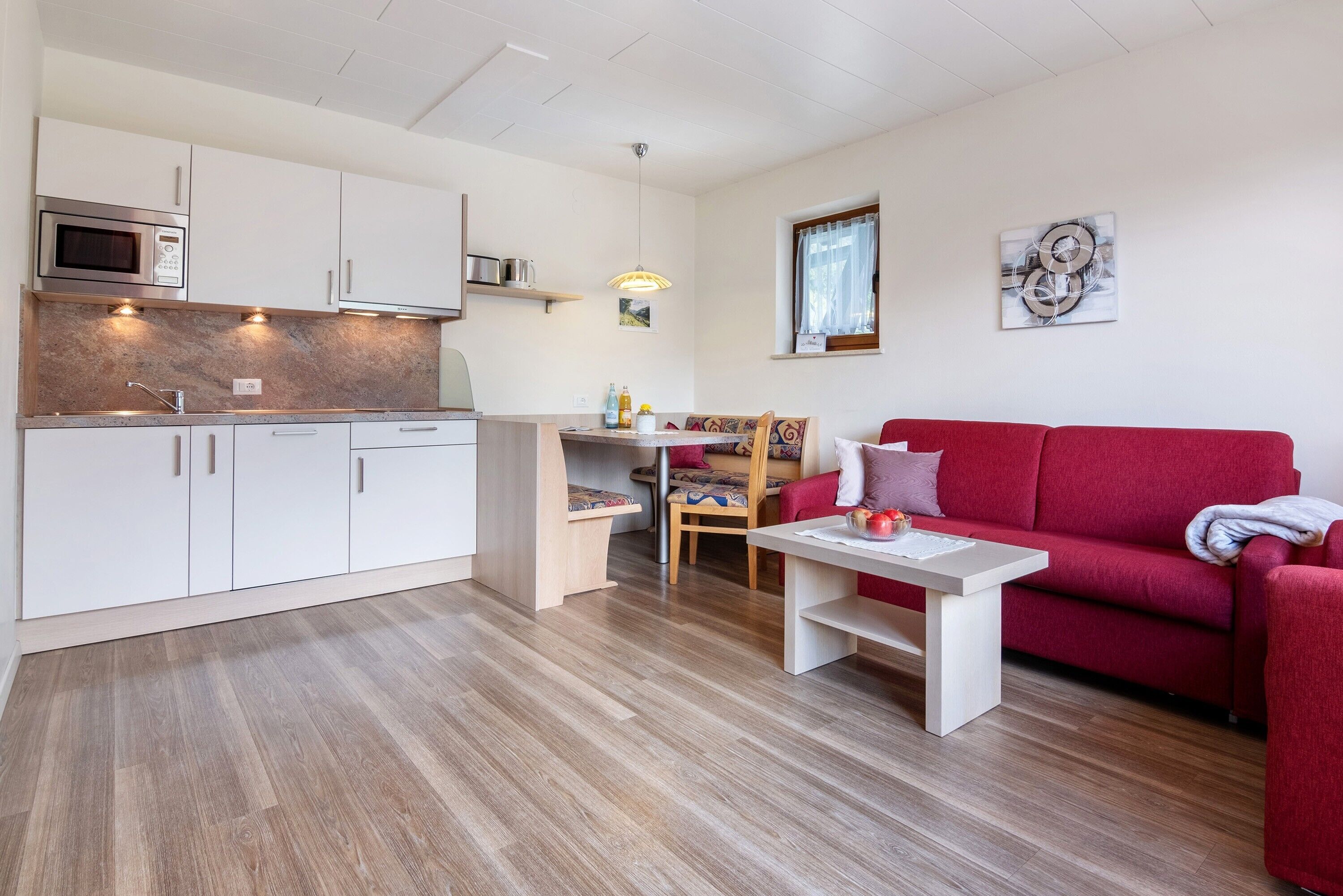 A compact living space with a kitchenette, a dining area, and a red sofa.