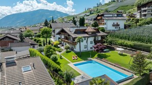 A residential property with a swimming pool, lush garden, and a mountainous backdrop.