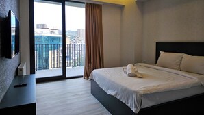 Une chambre d’hôtel moderne dotée d’un grand lit, d’un téléviseur à écran plat fixé au mur et d’un balcon offrant une vue sur la ville.
