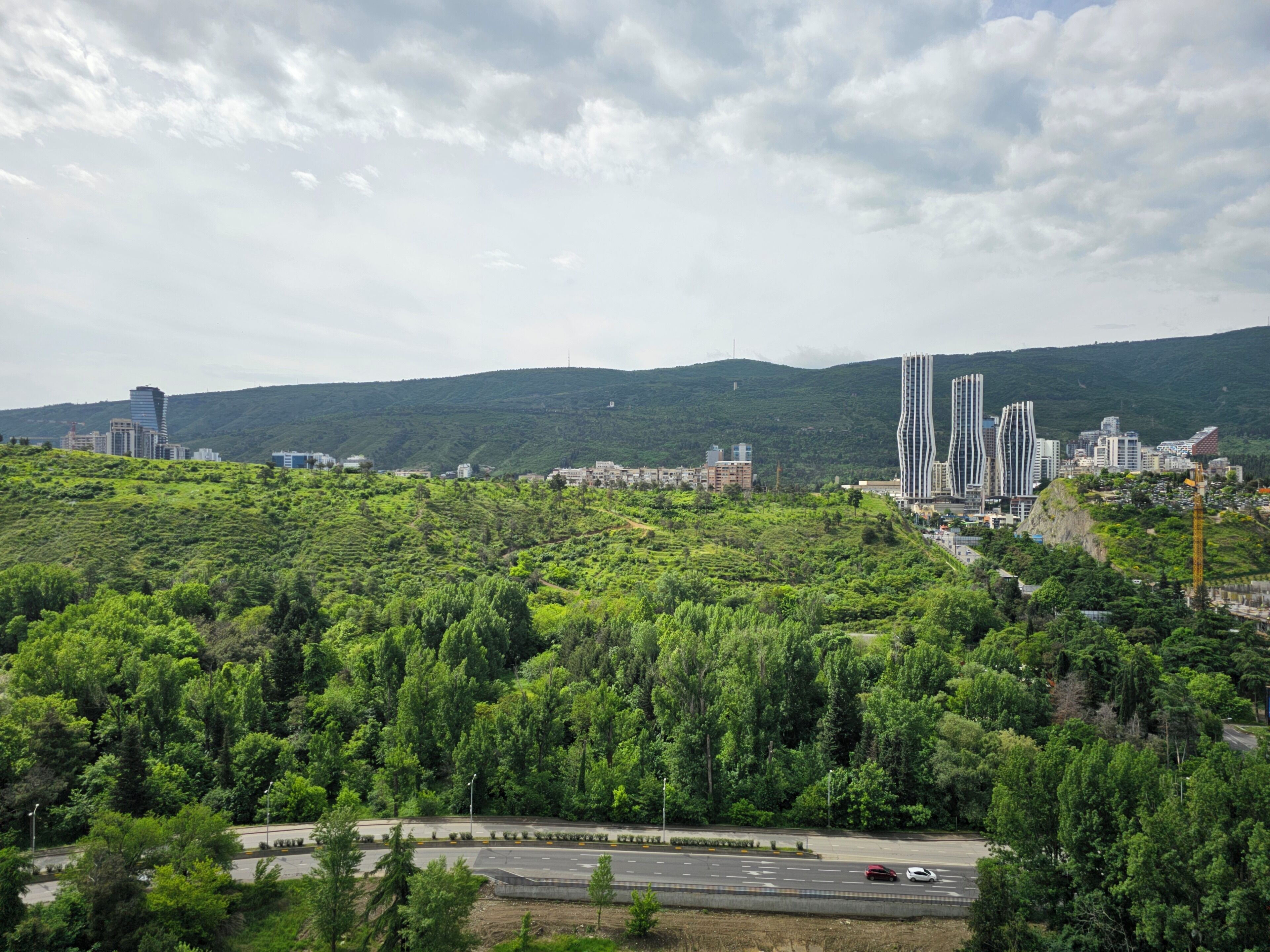 Un paysage urbain avec des bâtiments modernes, une autoroute et des collines verdoyantes.