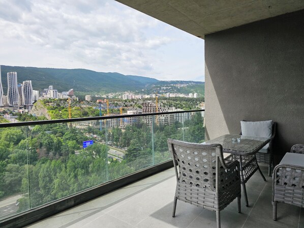 A balcony with a table and chairs, overlooking a cityscape with buildings and greenery. - Archi Tamarashvili (Tbilisi)