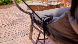 A hammock chair overlooking a patio with a wine bottle, glasses, and a table.
