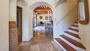 A hallway with stone flooring, wooden beams, and a staircase with a mirror.