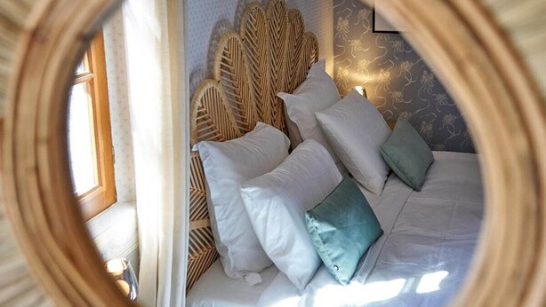 A bed with white and teal pillows, a woven headboard, and a circular mirror frame.