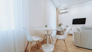 Ein modernes Wohnzimmer mit einem runden weißen Tisch, weißen Stühlen, einem grauen Sofa und einem an der Wand befestigten Flachbildfernseher.