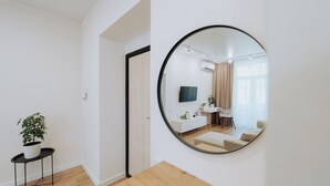 Ein modernes Wohnzimmer mit einem runden Spiegel, Holzboden, einem weißen Sofa, einem Fernseher und einer Topfpflanze.