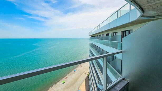 Un edificio alto con balcón que da a una playa y al océano.