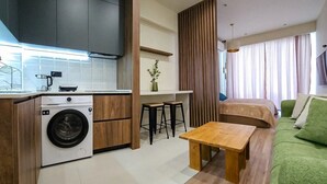 Un espacio habitable compacto con kitchenette, lavadora, zona de comedor y cama.