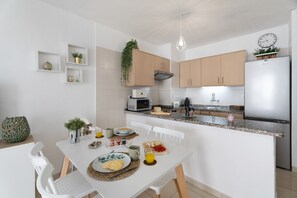 A modern kitchen with white cabinets, a stainless steel refrigerator, and a dining area with a white table and chairs.