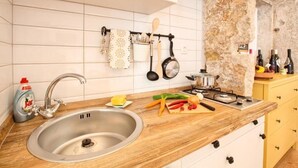 A kitchen with a stainless steel sink, wooden countertop, and a stone wall. There are various kitchen utensils and bottles on the wall. - Apartment Irma: Studio apartman (Pula)