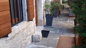 A narrow stone pathway leading to a building with wooden shutters and potted plants. - Apartment Irma: Studio apartman (Pula)